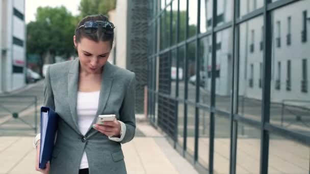 Geschäftsfrau zu Fuß und SMS auf dem Smartphone — Stockvideo
