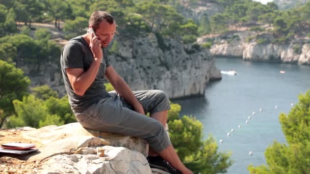 Человек, сидящий на скале и говорящий — стоковое видео