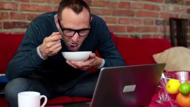 Чоловік з ноутбуком їсть суп — стокове відео
