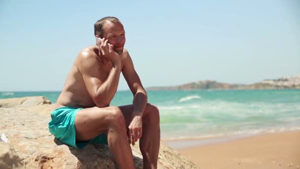 Мужчина разговаривает по сотовому на пляже — стоковое видео