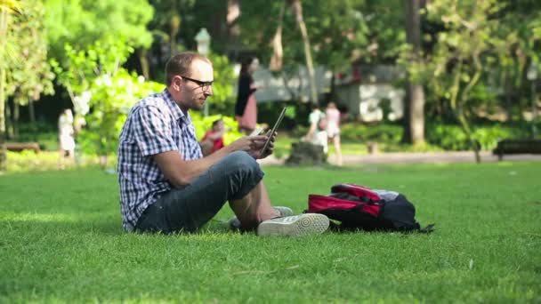 Студент с помощью смартфона и планшета в парке — стоковое видео