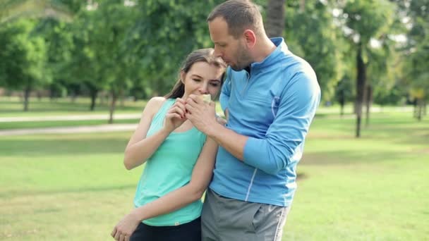 Deportiva pareja comiendo manzana hablando en el parque — Vídeo de stock