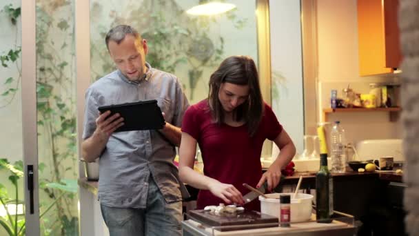 Женщина готовит еду и мужчина просматривает веб — стоковое видео