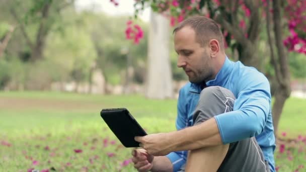 Спортсмен використовує планшет на траві — стокове відео