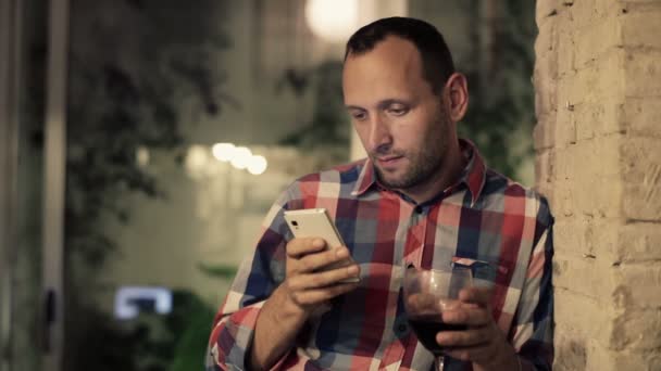 Человек пьет вино и пишет смс на смартфоне — стоковое видео