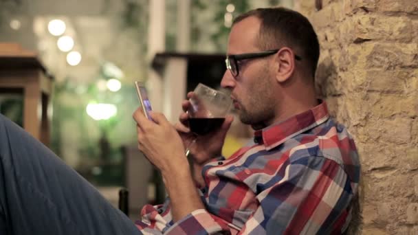 Hombre bebiendo vino y mensajes de texto en el teléfono inteligente — Vídeo de stock