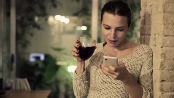 Frau schreibt SMS auf Smartphone und trinkt Wein — Stockvideo