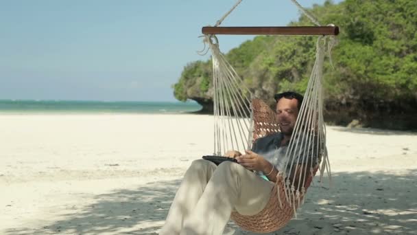 Άνθρωπος με laptop χαλαρώνοντας στην αιώρα στην εξωτική παραλία — Αρχείο Βίντεο