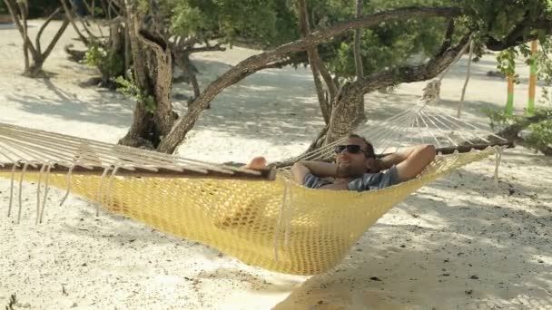Молодой счастливый человек лежит, расслабляясь на гамаке — стоковое видео