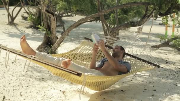 Young man reading book while lying, relaxing on hammock — Stock Video