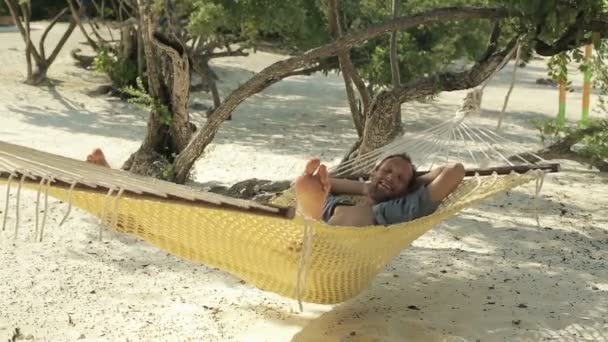 Молодий щасливий чоловік посміхається до камери, лежачи на гамаку — стокове відео