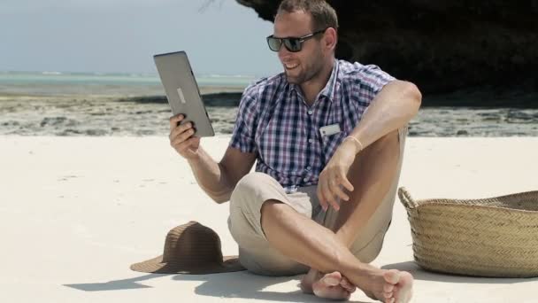 Hombre joven en la playa exótica charlando en la computadora tableta — Vídeos de Stock