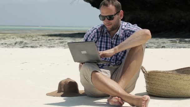 Young man working on laptop on beautiful exotic beach — Stock Video