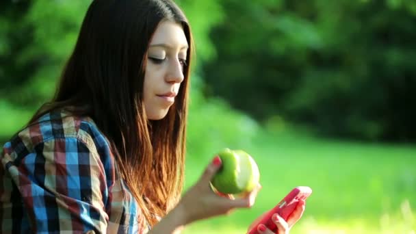 Teenager schreiben SMS auf Smartphone, essen Apfel — Stockvideo