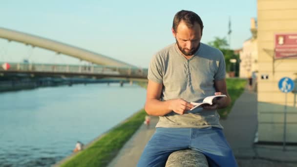 Man die leest boek over muur door rivier — Stockvideo