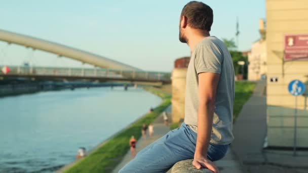 Depressed man sitting on wall by river — Stock Video