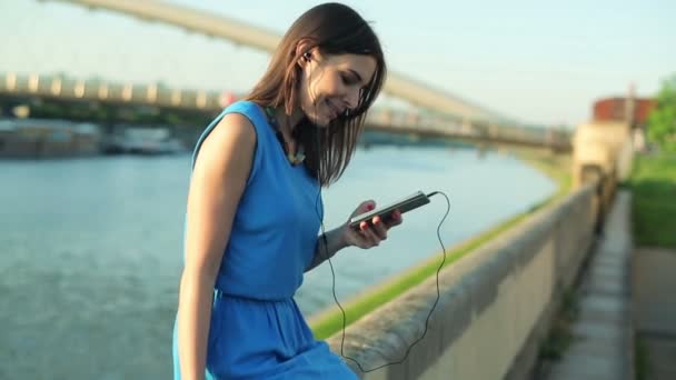 Vrouw luisteren muziek op smartphone door rivier — Stockvideo