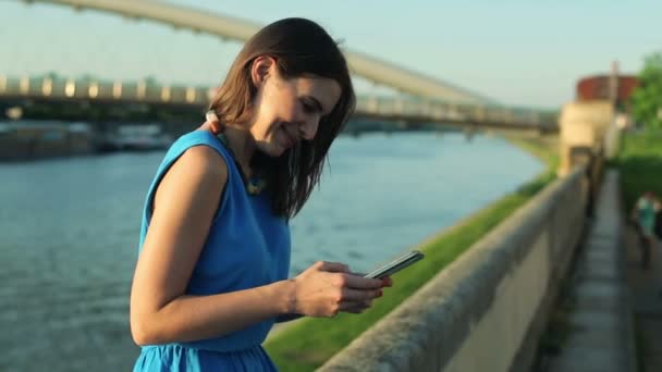 Женщина пишет смс на смартфоне у реки — стоковое видео