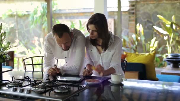 Couple regardant des photos sur tablette dans la cuisine — Video