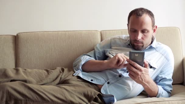 Man het texting, sms verzenden op sofa — Stockvideo