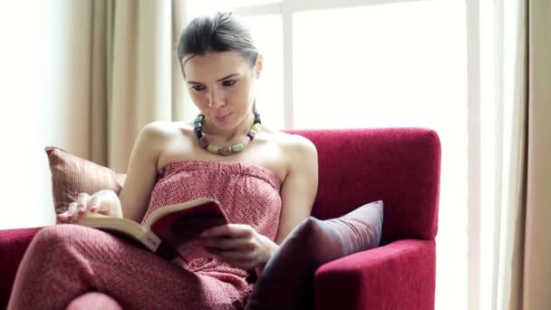 Mujer leyendo libro en sillón — Vídeos de Stock