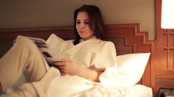 Mujer leyendo el periódico acostada en la cama — Vídeos de Stock