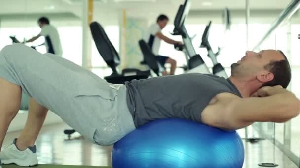 Hombre haciendo ejercicio en la pelota de fitness en el gimnasio — Vídeos de Stock