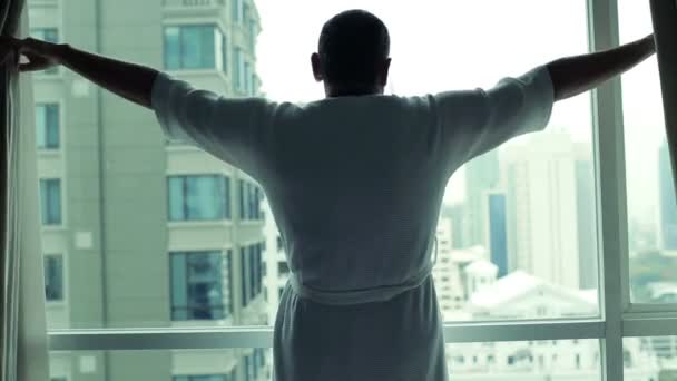 Чоловік розкриває штори в готельному номері — стокове відео