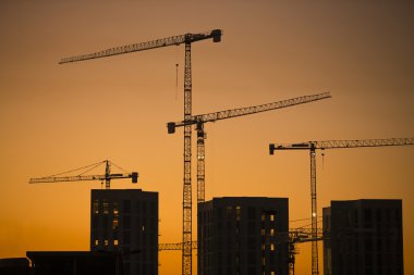 gün batımında Vinçler. Endüstriyel İnşaat vinçleri ve sunrise sun üzerine bina silhouettes.