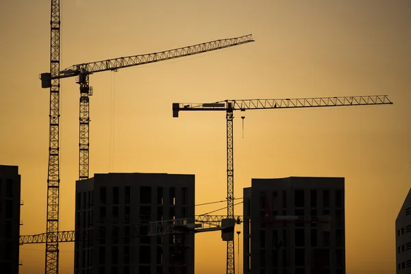 Gru al tramonto. Gru industriali da costruzione e sagome di edifici al sole all'alba . — Foto Stock