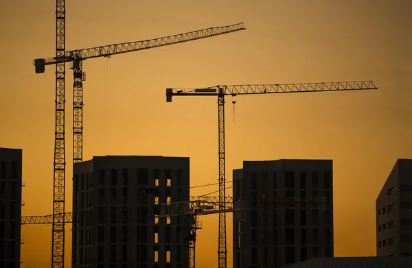 Gru al tramonto. Gru industriali da costruzione e sagome di edifici al sole all'alba . — Foto Stock