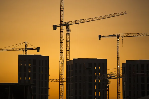 Gru al tramonto. Gru industriali da costruzione e sagome di edifici al sole all'alba . — Foto Stock