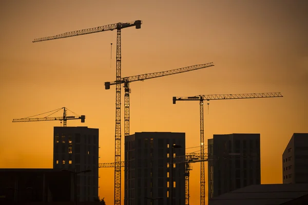 Gru al tramonto. Gru industriali da costruzione e sagome di edifici al sole all'alba . — Foto Stock