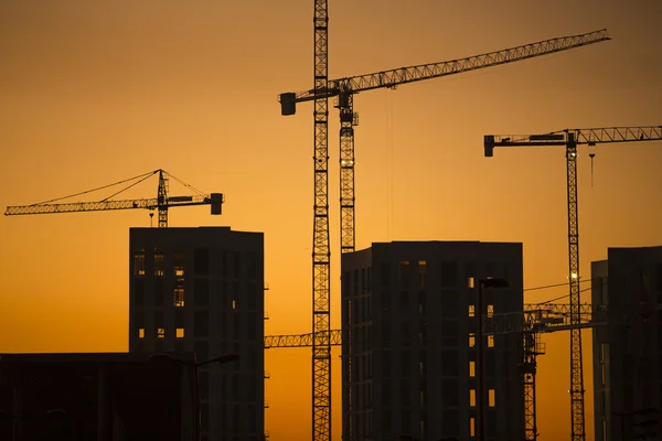 Cranes at sunset. Industrial construction cranes and building silhouettes over sun at sunrise. — Stock Photo, Image