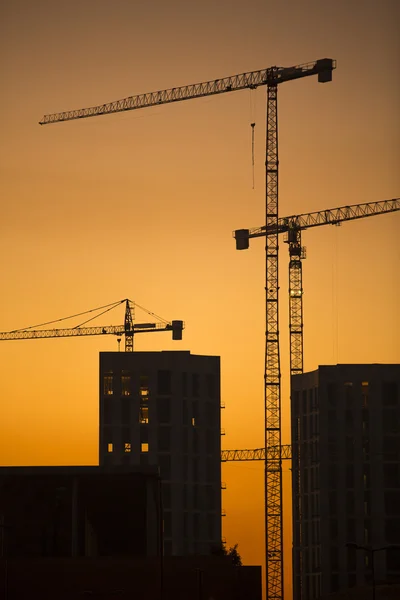 Cranes at sunset. Industrial construction cranes and building silhouettes over sun at sunrise. In vertical format. — Stock Photo, Image