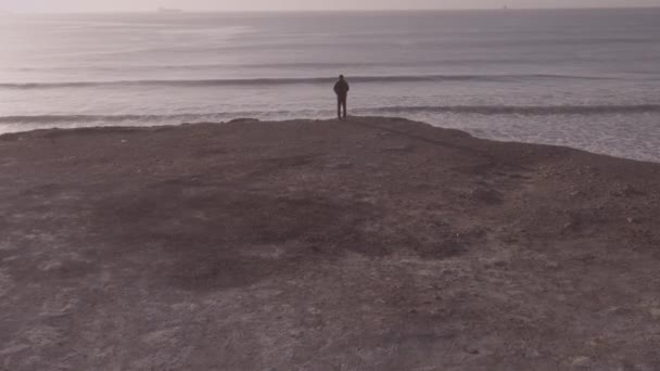 Letecký pohled na muže stojícího na útesu s dronem letícím k oceánu — Stock video