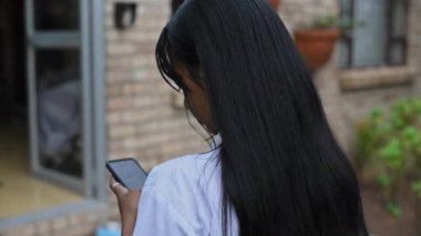 Cep telefonunu kullanan genç bir kadının arka görüntüsü.