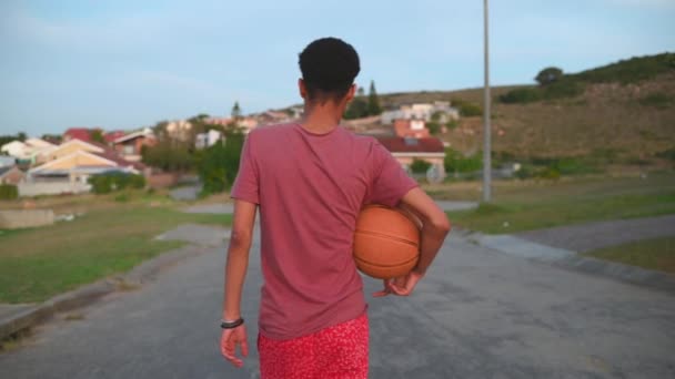Bakifrån av ung pojke promenader med basket på gatan — Stockvideo