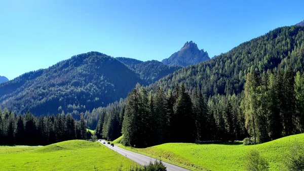 Light traffic on the road that runs through the Braies valley passing alongside large forest. In the background, Mount Pollice, Daumkofel, of 2259 meters