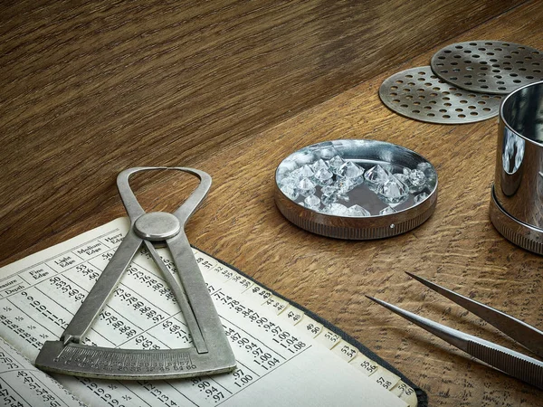 Antique Diamond Tools. Loose diamonds, measuring gauge and diamond sieve plates on dark wooden background. 
