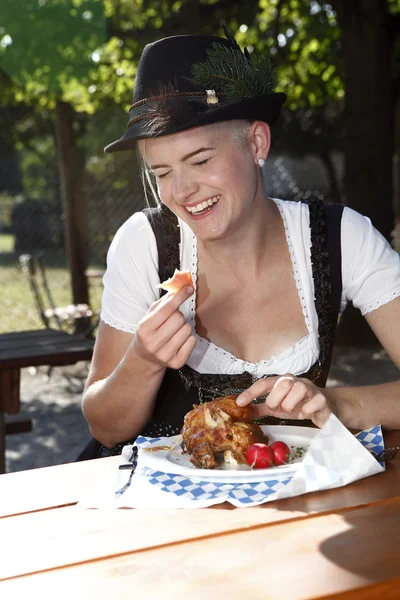 Blonde fille mange moitié poulet dans un jardin de bière traditionnelle — Photo