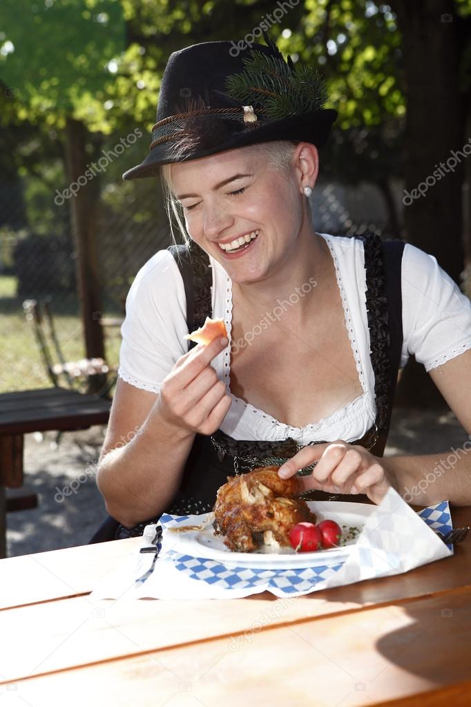 Blonde girl eats half chicken in a traditional beer garden