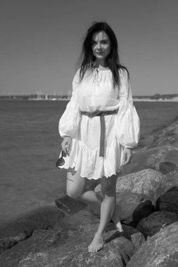Deniz kenarındaki genç, narin kadın. Kıyafetler içinde poz veriyor.