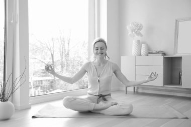 Genç ve güzel bir kadın büyük pencerenin yanında yoga yapıyor.