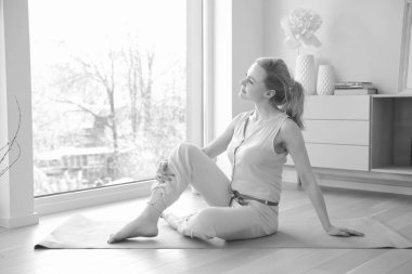 Genç ve güzel bir kadın büyük pencerenin yanında yoga yapıyor.