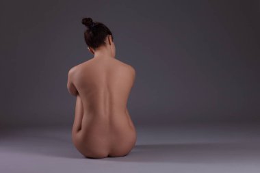 Karanlık bir arka planda çıplak poz veren seksi genç kadın.