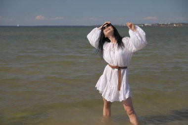 Deniz kenarındaki genç, narin kadın. Kıyafetler içinde poz veriyor.