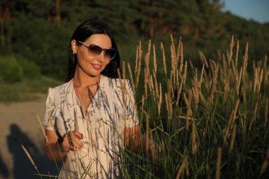 Çimlerin üzerinde elbise giymiş genç bir kadının portresi.
