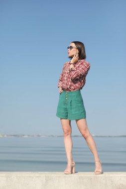 Deniz kenarındaki genç, narin kadın. Kıyafetler içinde poz veriyor.