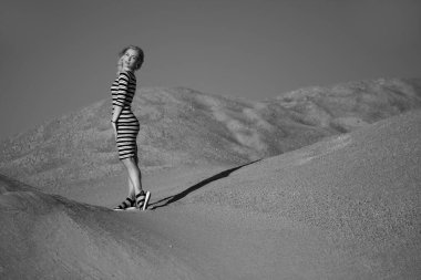 Genç bir kadın kumlu dağda elbise giymiş poz veriyor.